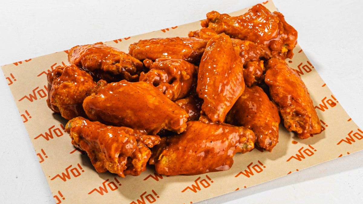 A pile of spicy chicken wings covered in red sauce on wings over branded paper